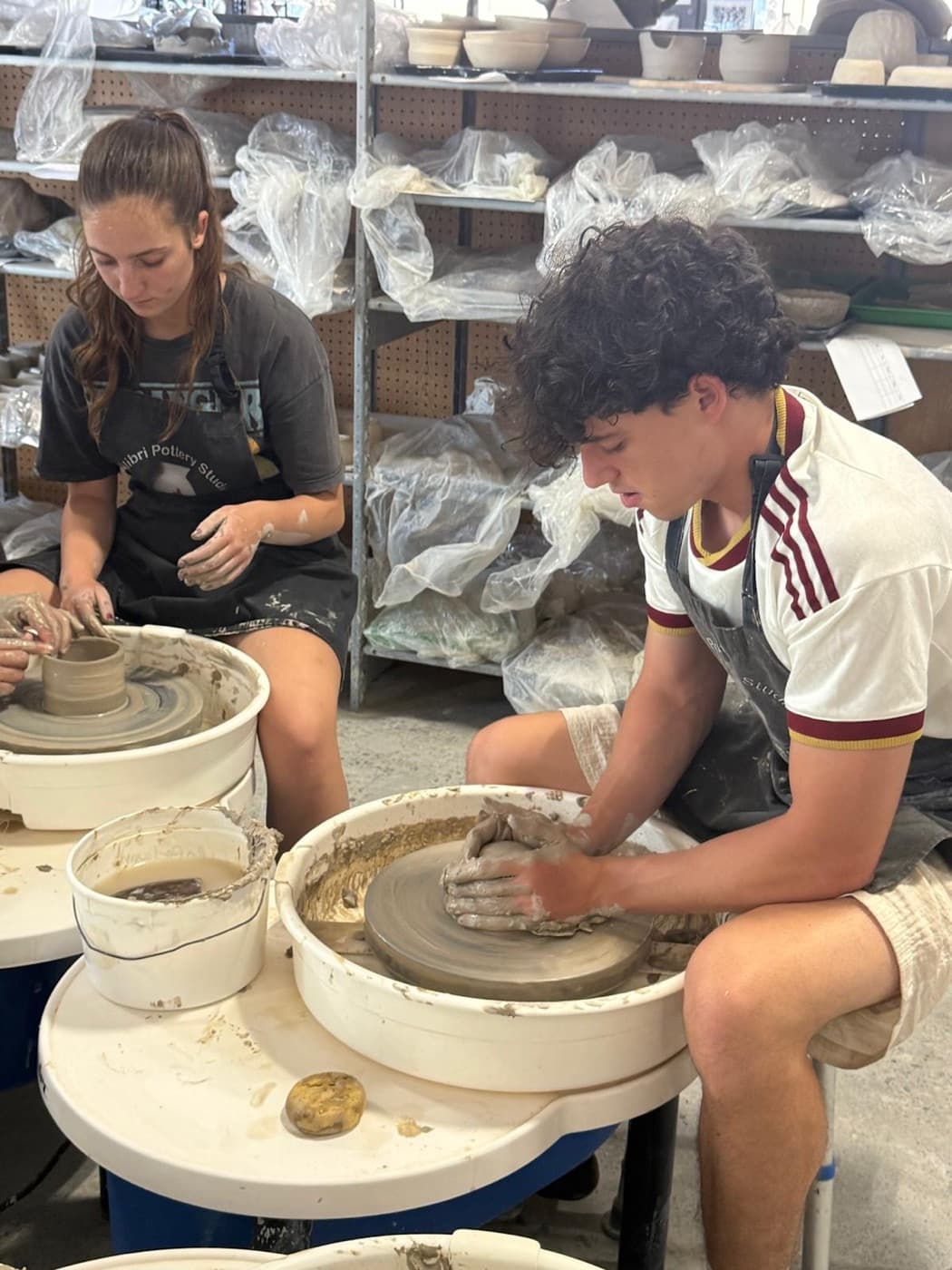 Two students shaping bowls on the pottery wheel during a class