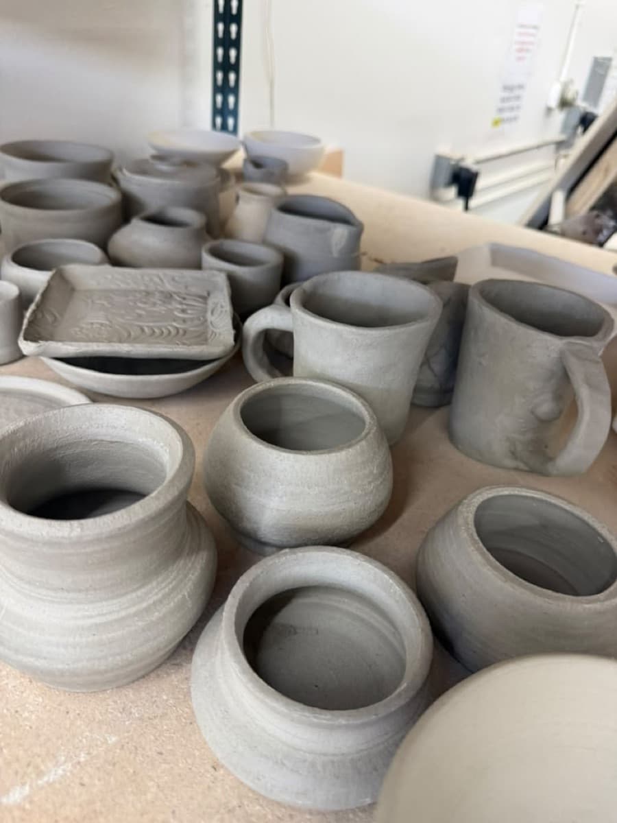 Freshly made mugs, cups and a carved dish drying before their first firing